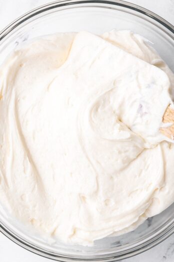 Square image of Buttercream frosting in a bowl with a rubber spatula dipped in.