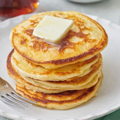 Stack of fluffy greek yogurt pancakes with a pat of butter on top.