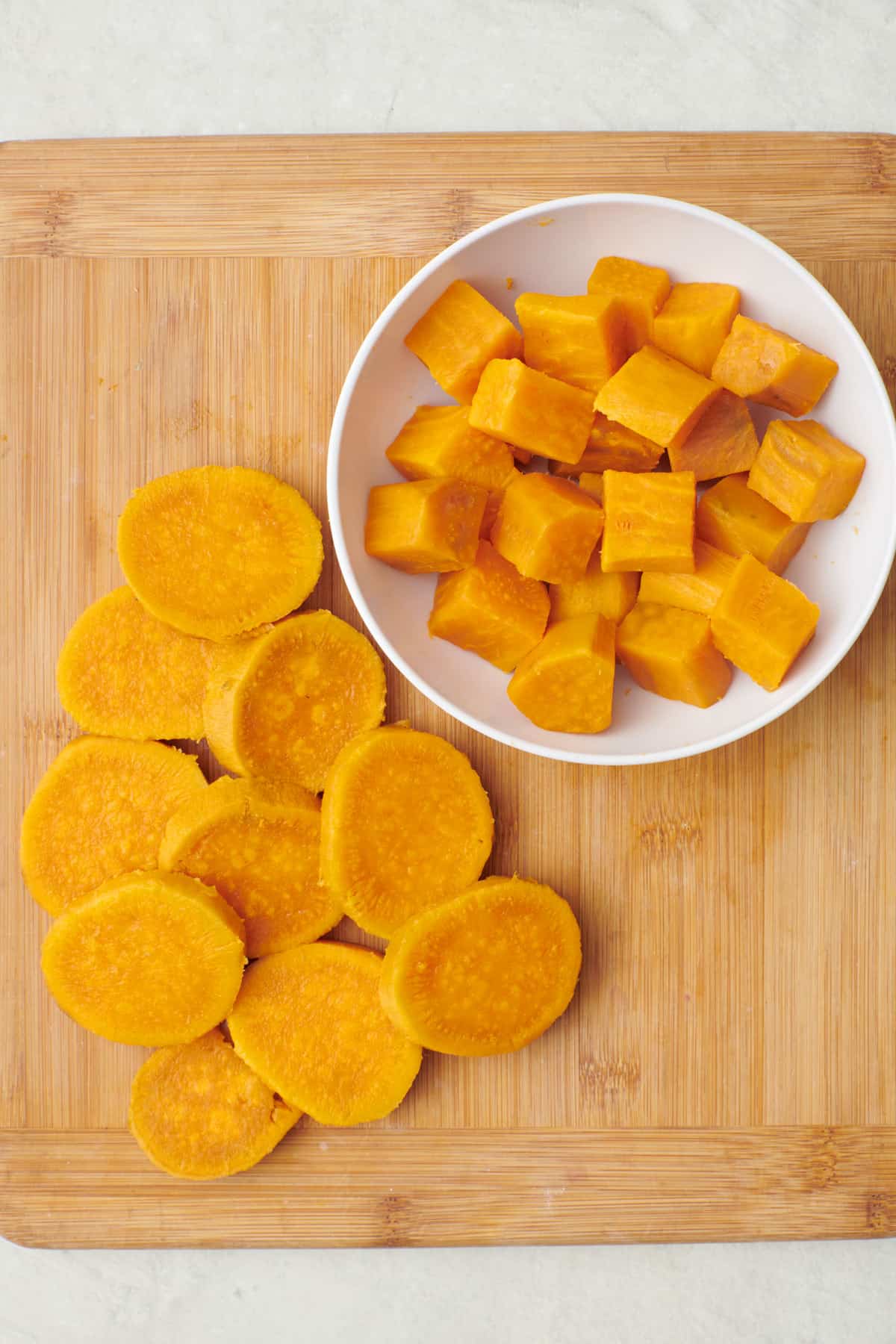 Sweet potatoes cut into round and cubes on a cutting board after boiling.