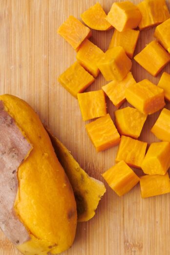 Boiled sweet potatoes on a cutting board 2 ways: whole and cubed.