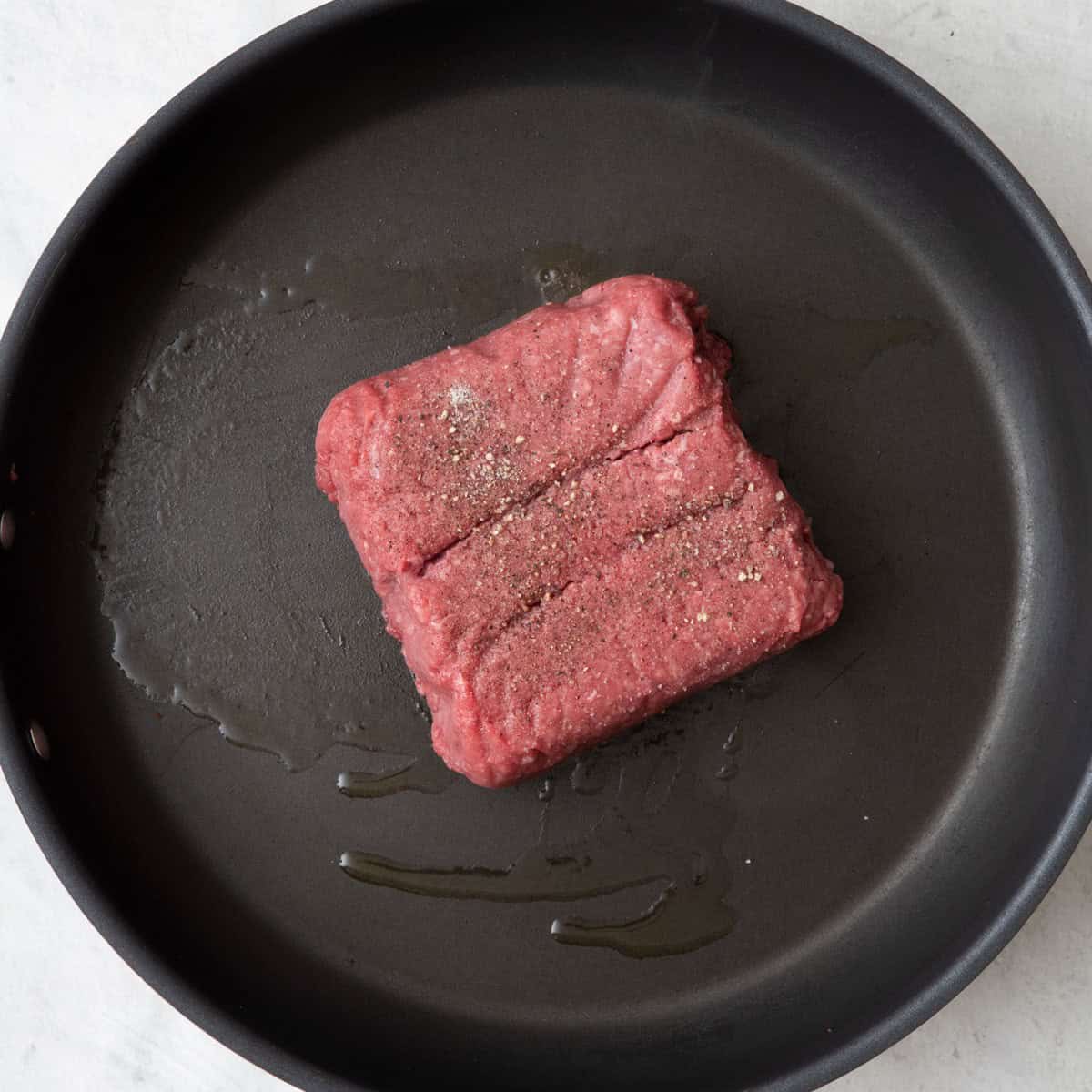 Ground beef block on skillet with oil.