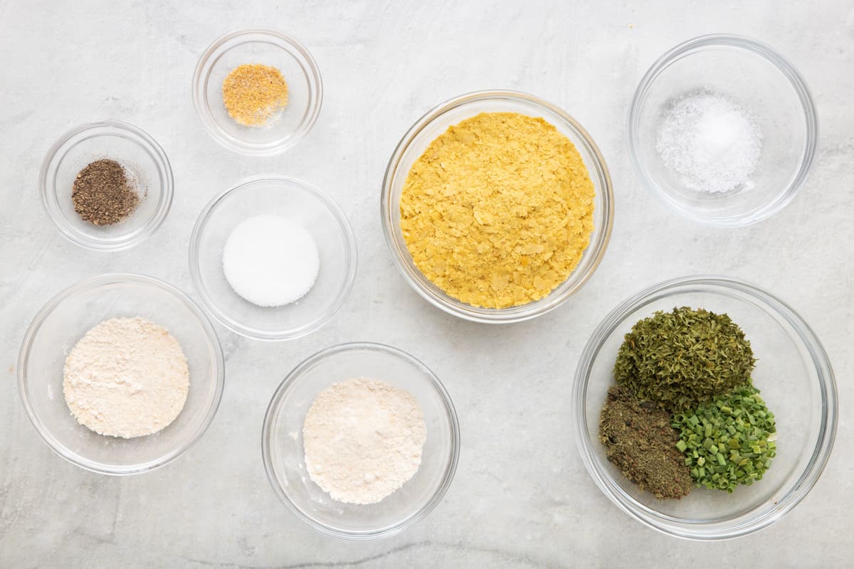 Ingredients for recipe in individual bowls: dried buttermilk powder, dried parsley, dill, and chives, onion powder, garlic powder, sugar, mustard powder, black pepper, and salt.