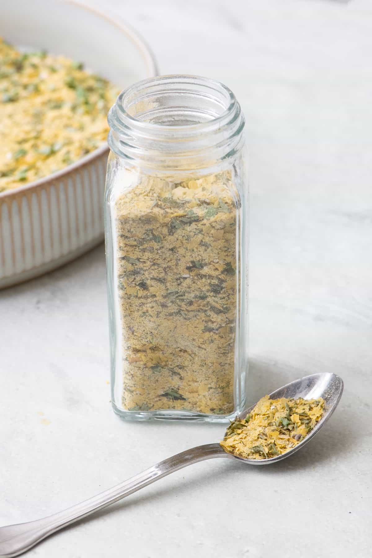Ranch seasoning in a spice jar with a spoon with some on it and bowl of seasoning nearby.