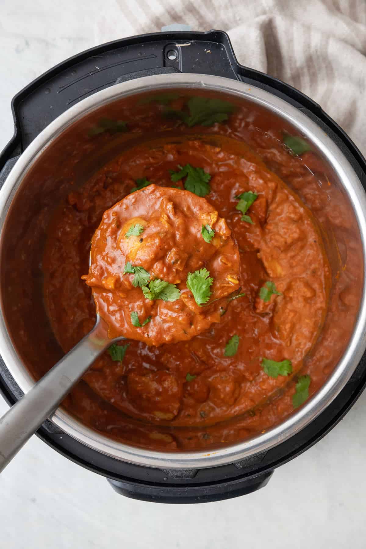 Instant pot butter chicken in the pot being lifted up with a ladle and garnished with fresh cilantro.