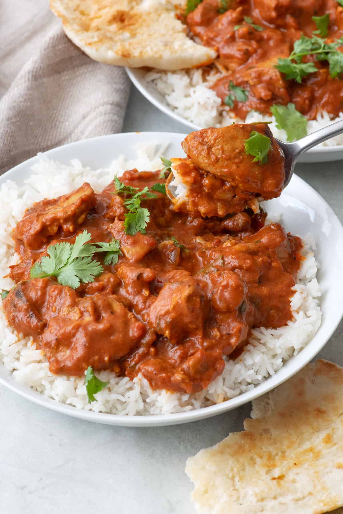 Spoon lifting up a bite of butter chicken over rice.