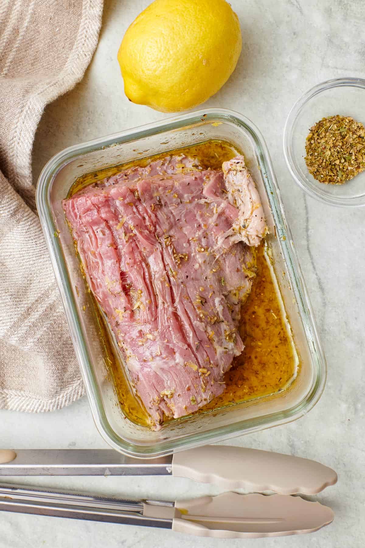 Flake steak in a small glass dish coated in a lemony Italian marinade.