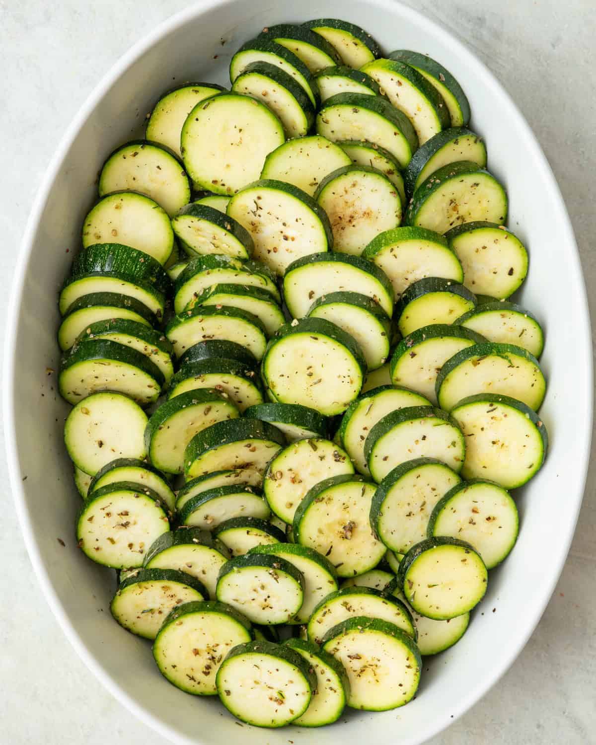Zucchini in a baking dish tossed with oil and seasonings.