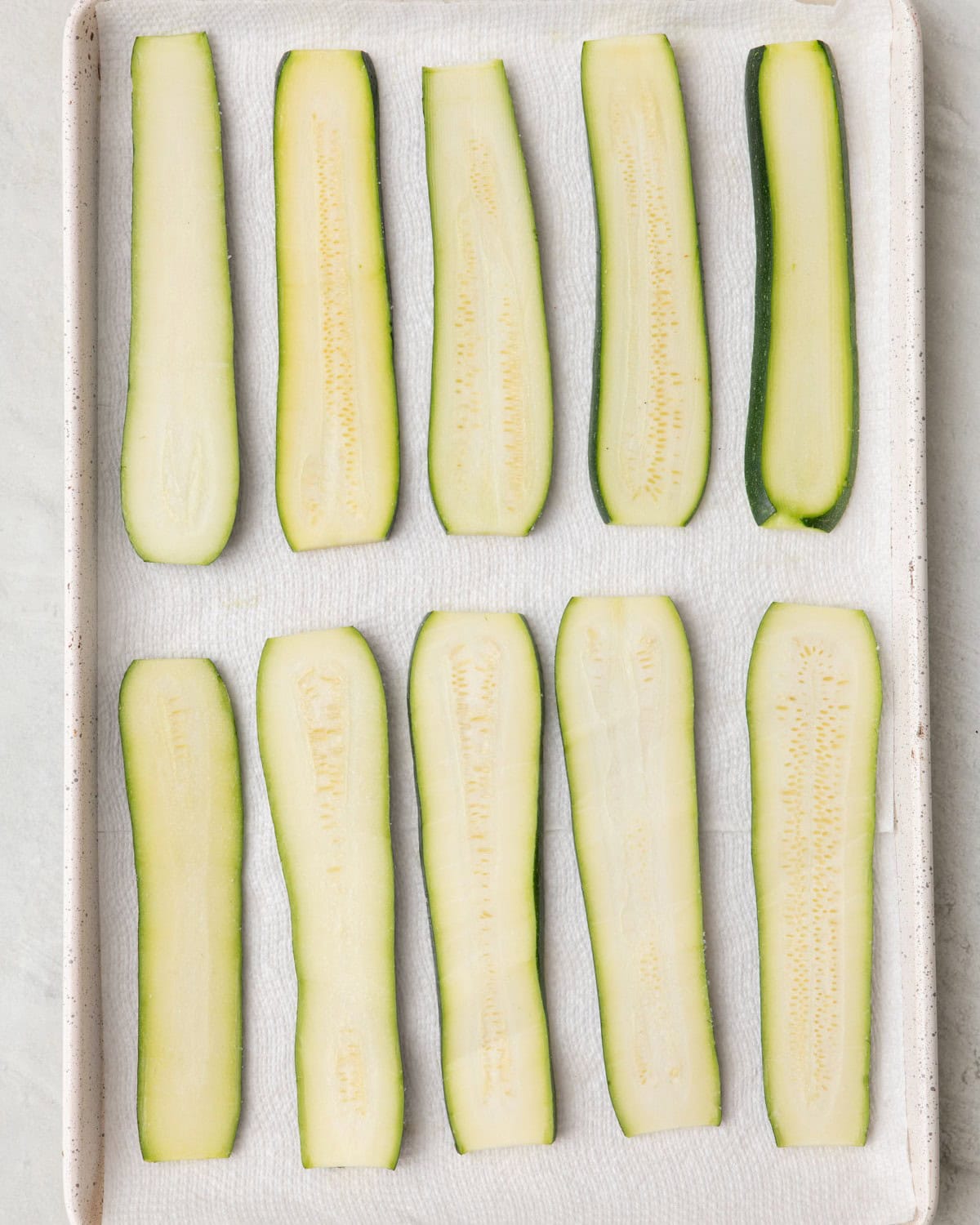 Paper towel lined sheet pan with a layer of zucchini planks with salt sprinkled on top.