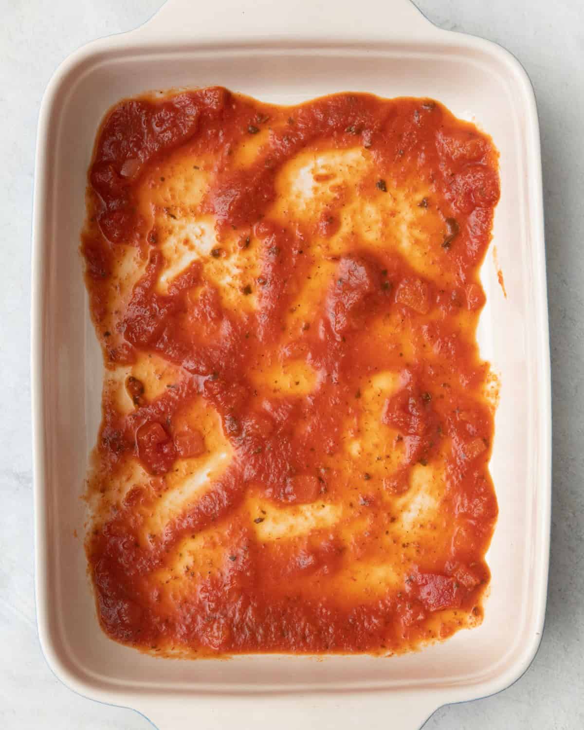 Marinara added to the bottom of a baking dish.