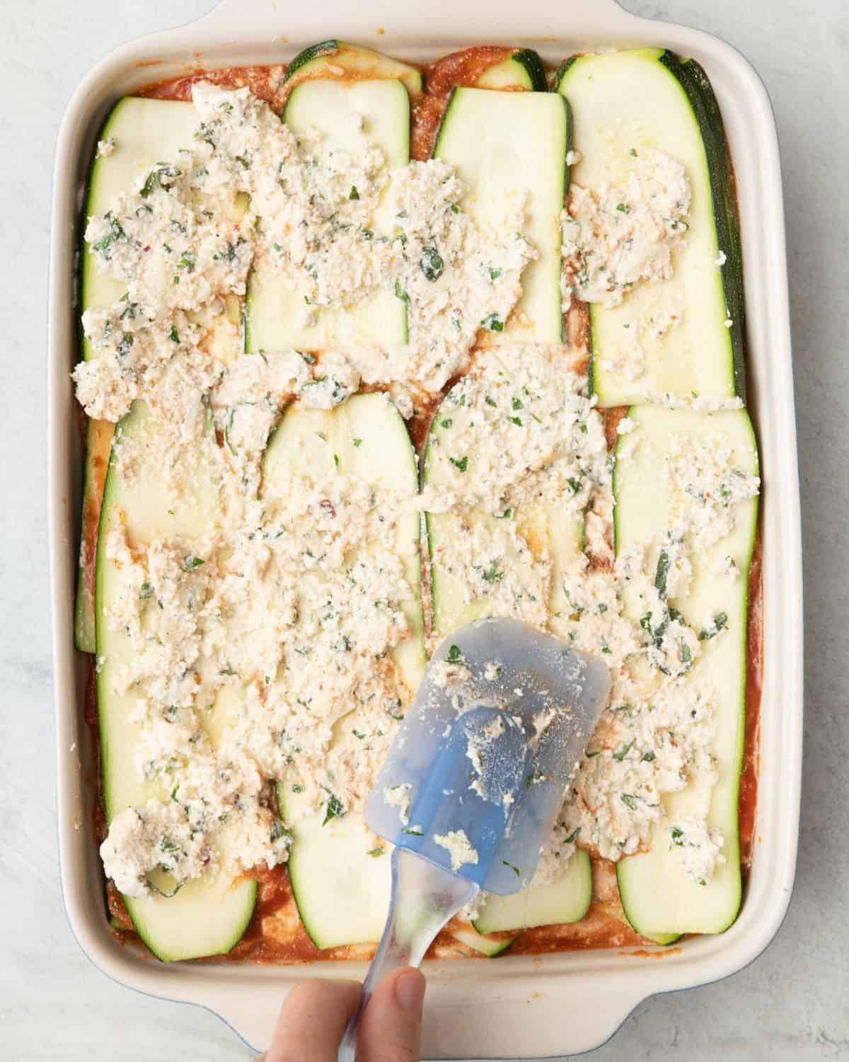 Spreading ricotta over final layer of zucchini planks.