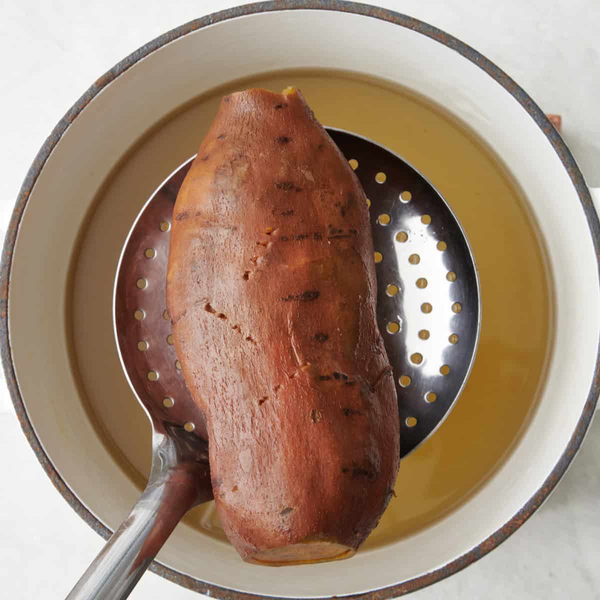 Potato after cooking, being removed from the water with a slotted spoon.