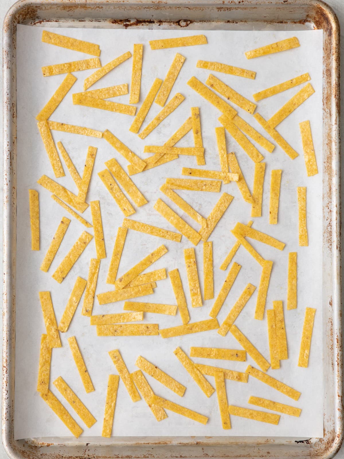 Tortilla strips tossed with oil on a baking sheet before baked.