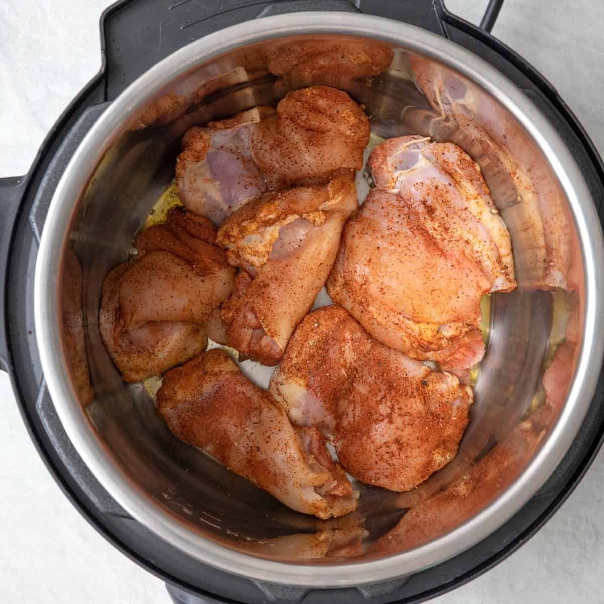 Seasoned chicken thighs in IP before cooked showing seasoning.
