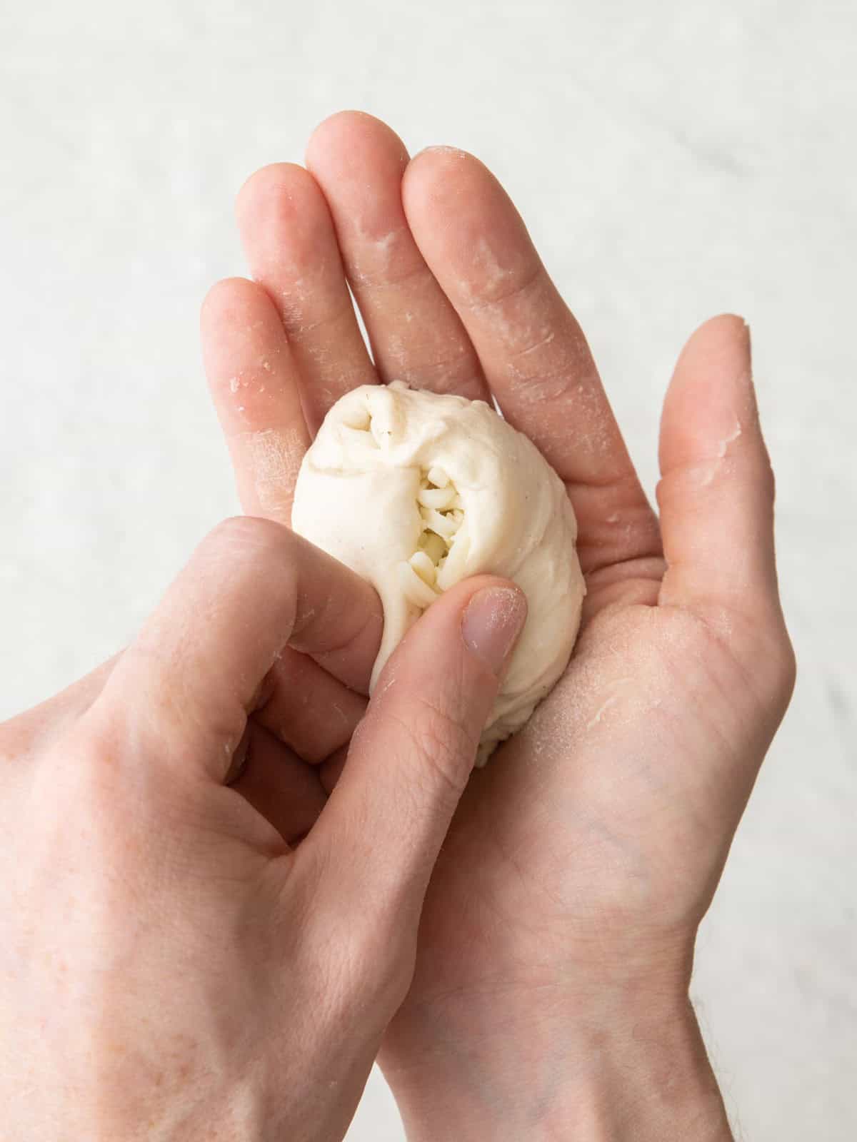 Hands forming the dough around the cheese.
