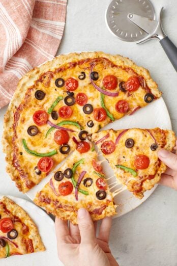 Chicken crust pizza with hand pulling two slices apart.
