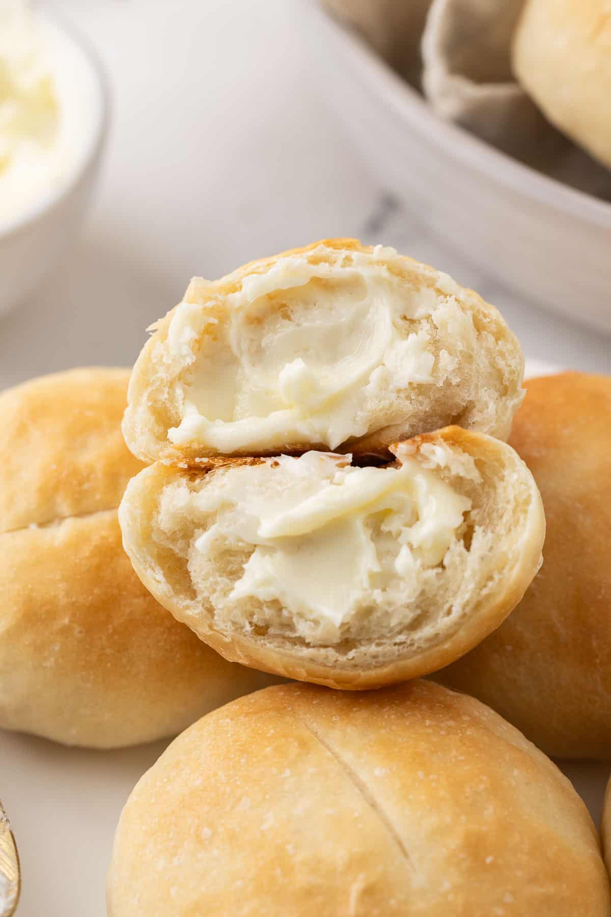French bread roll cut in half and smeared with butter sitting on top of more rolls.