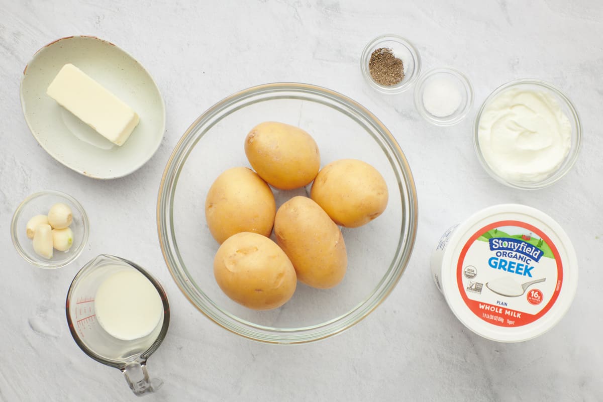 Ingredient for recipe: butter, garlic, milk, potatoes, salt and pepper, and Stonyfield Whole Milk Organic Greek Yogurt in a bowl and tub.