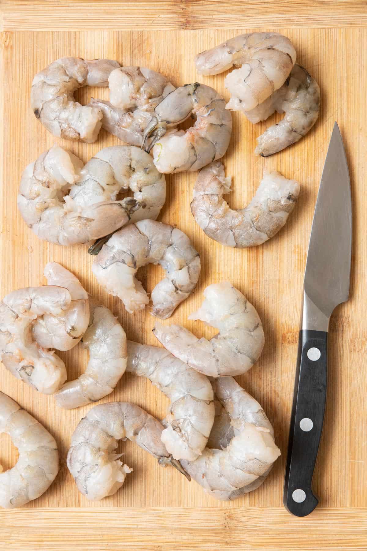 Peeled and deveined shrimp on a cutting board with a pairing knife.