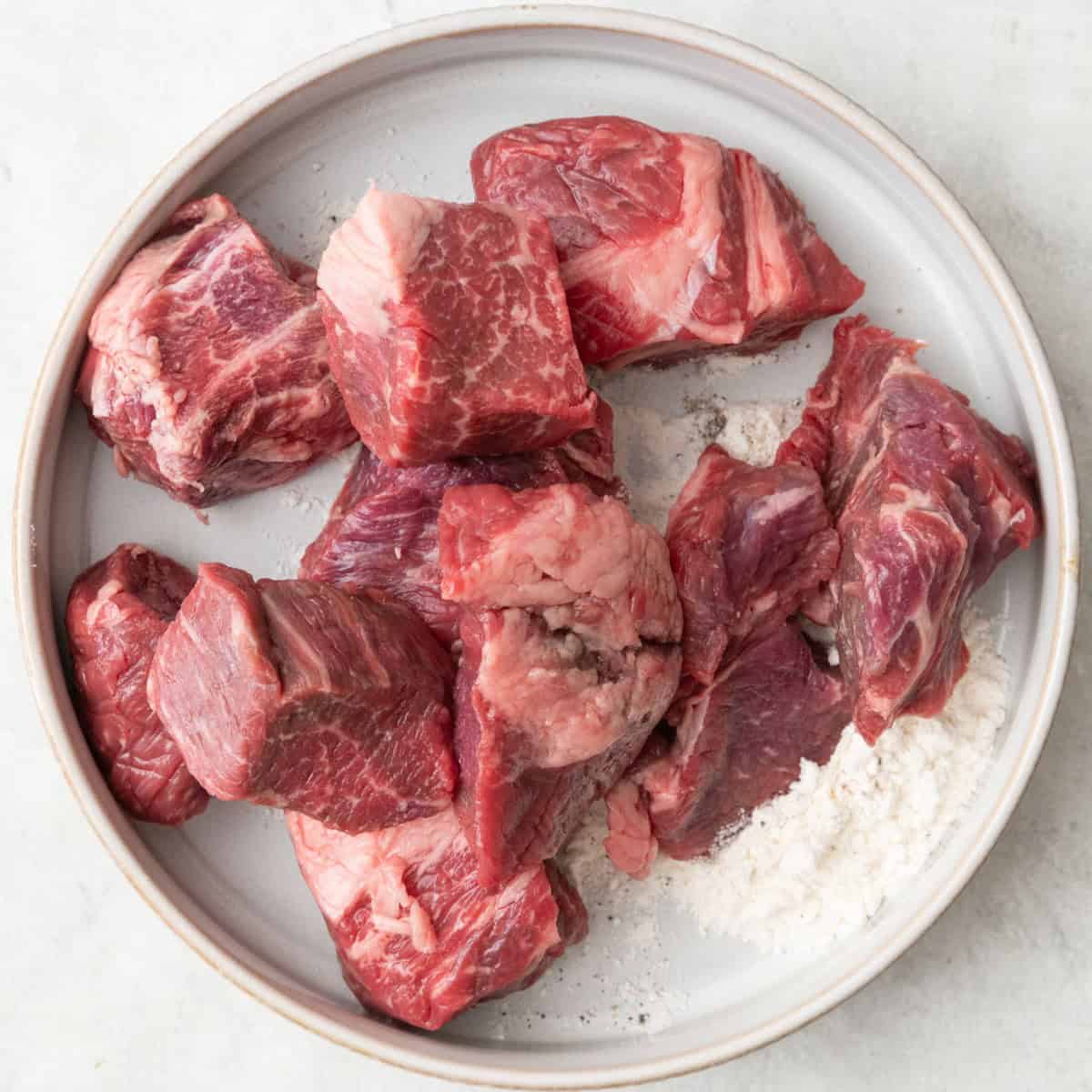 Flour, salt, and pepper in a shallow bowl with beef added.
