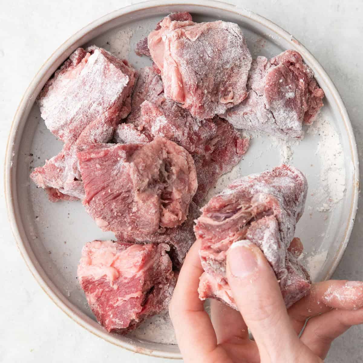 Hand tossing beef in flour to evenly coat.