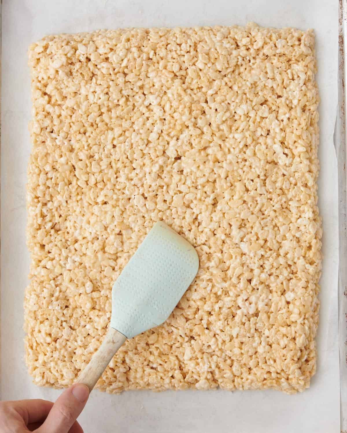 Mixture in parchment lined baking sheet with a spatula pressing into an even layer.