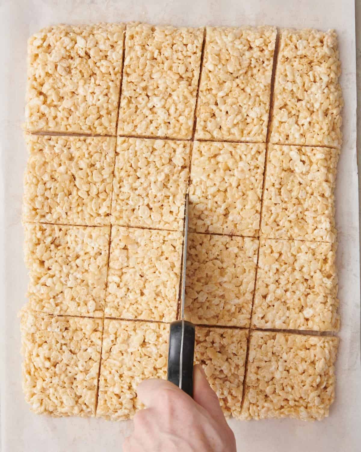 Cutting the rice krispie treats on large cutting board with parchment .