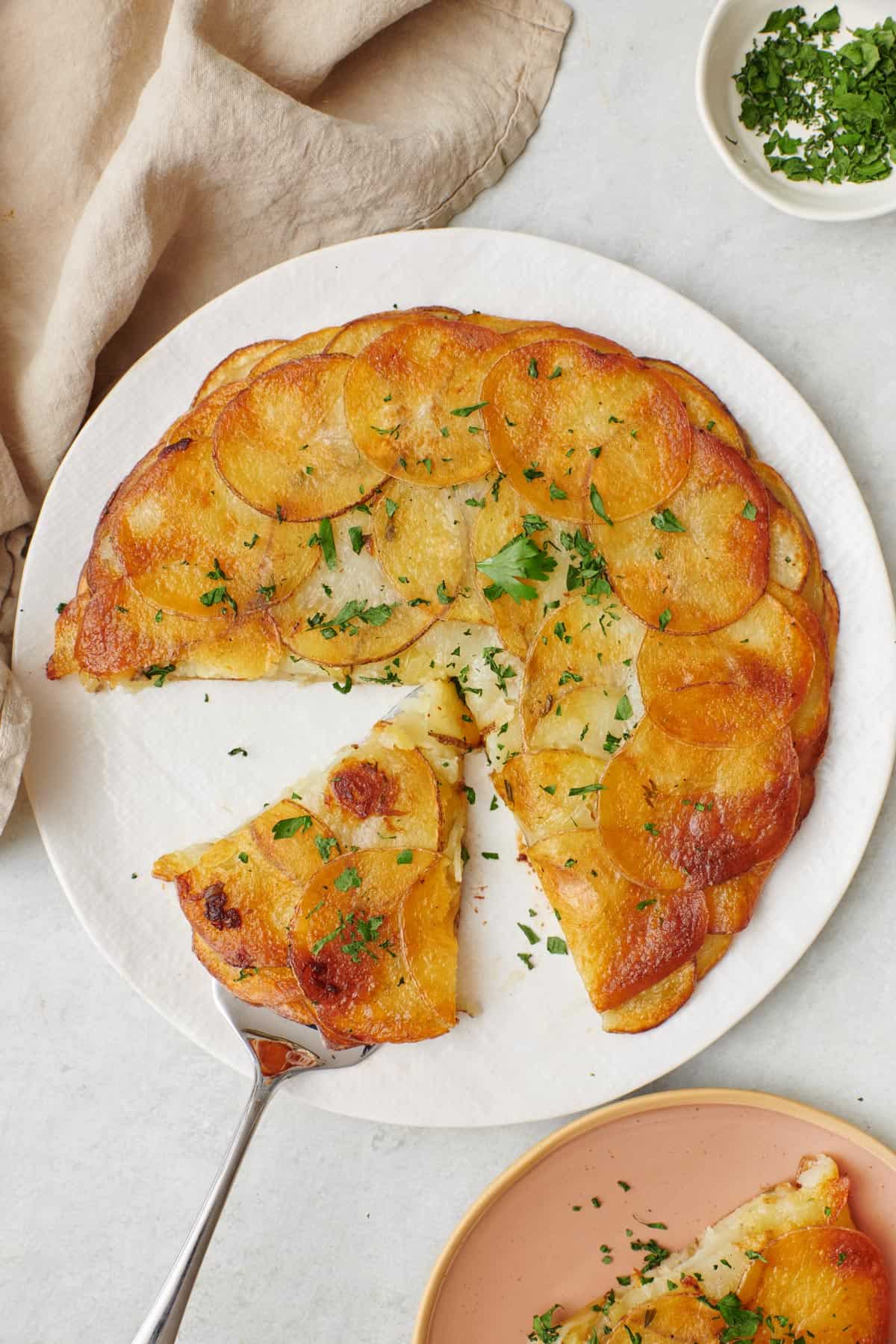 Potato galette with a few slices cut out, one on a spatula on the plate with another serving on a small plate nearby.