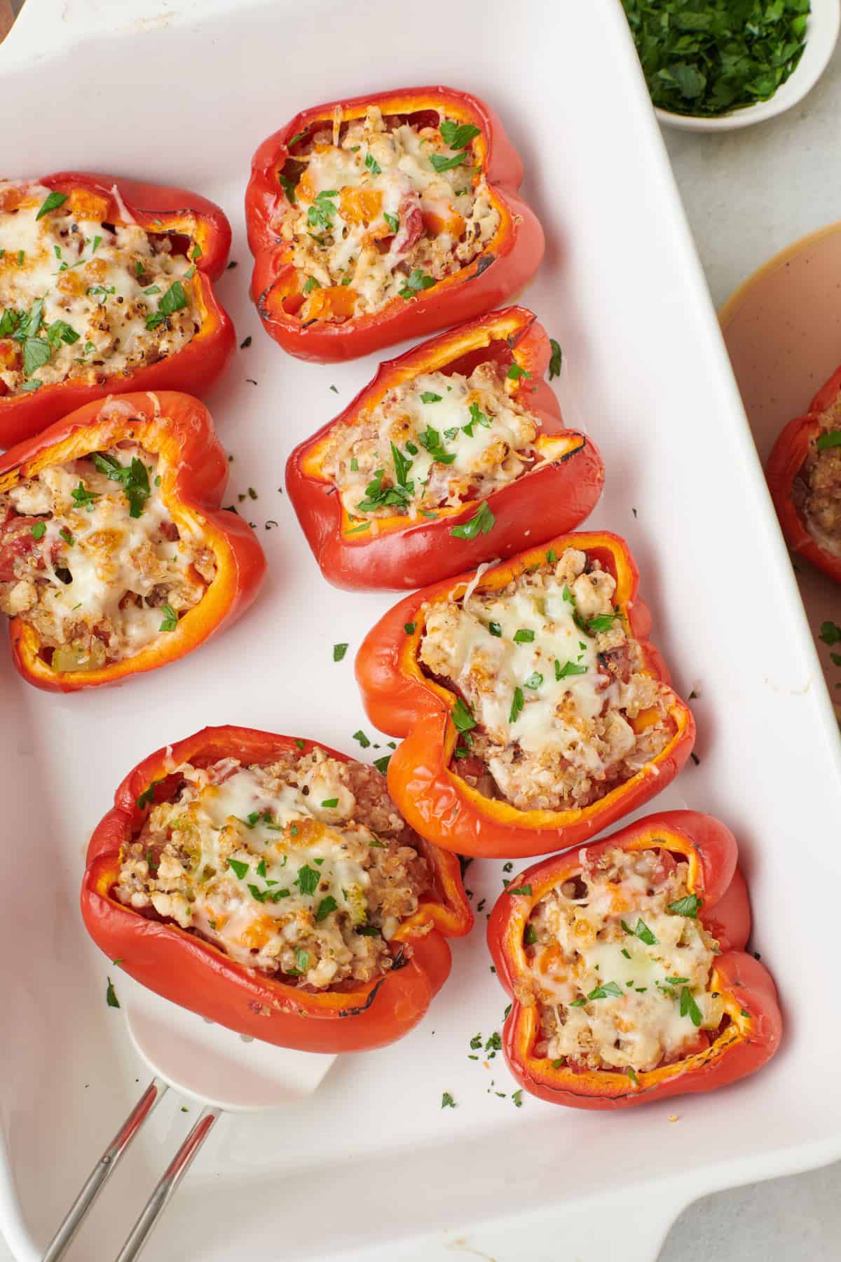 Turkey stuffed peppers in baking dish, garnished with fresh parsley with one pepper removed onto a plate with spatula resting inside dish.