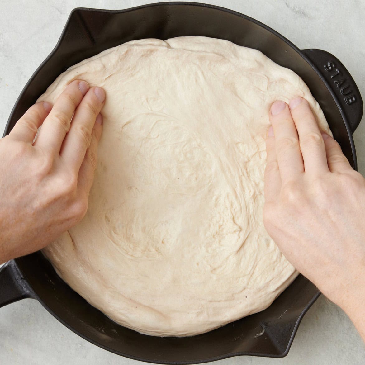 Hands stretching out pizza dough into a 10 inch round, mostly formed.