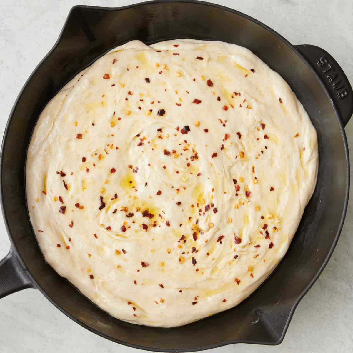 Dough in a cast iron stretched out to the edges with pepper and oil added.