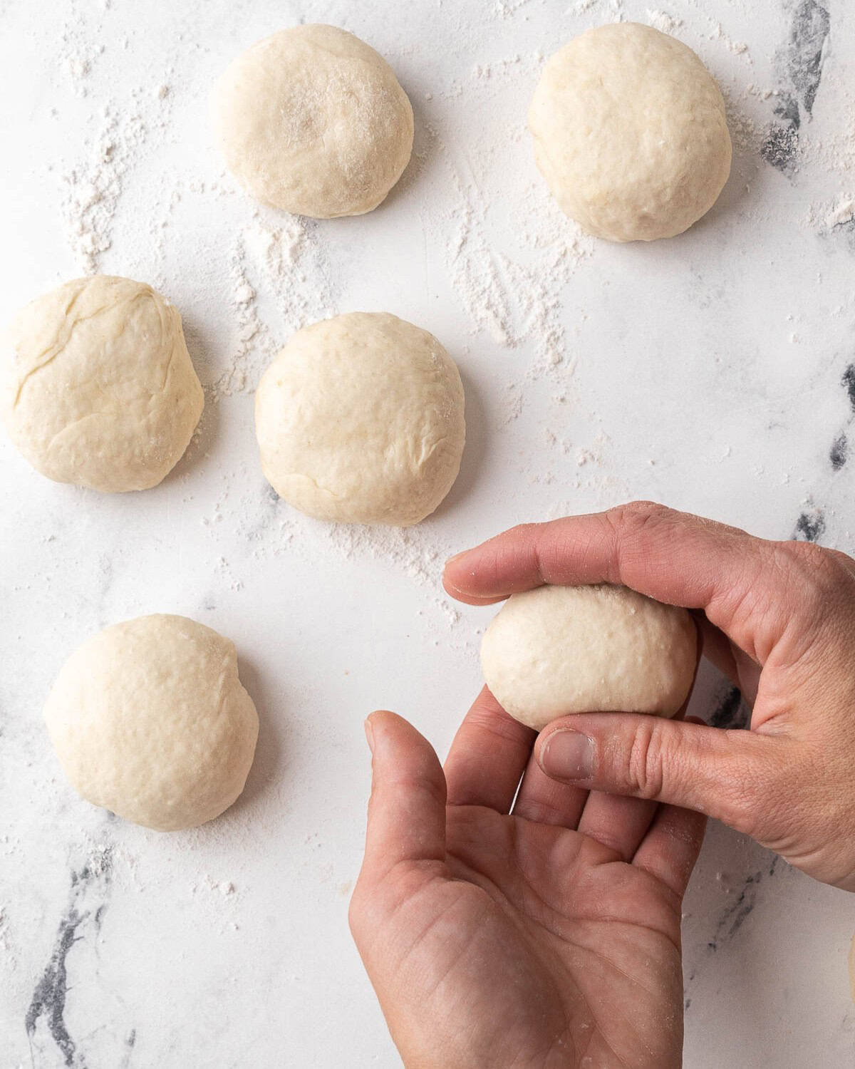 Hand rolling a piece of dough on the surface into a ball with a few dough balls already formed nearby.