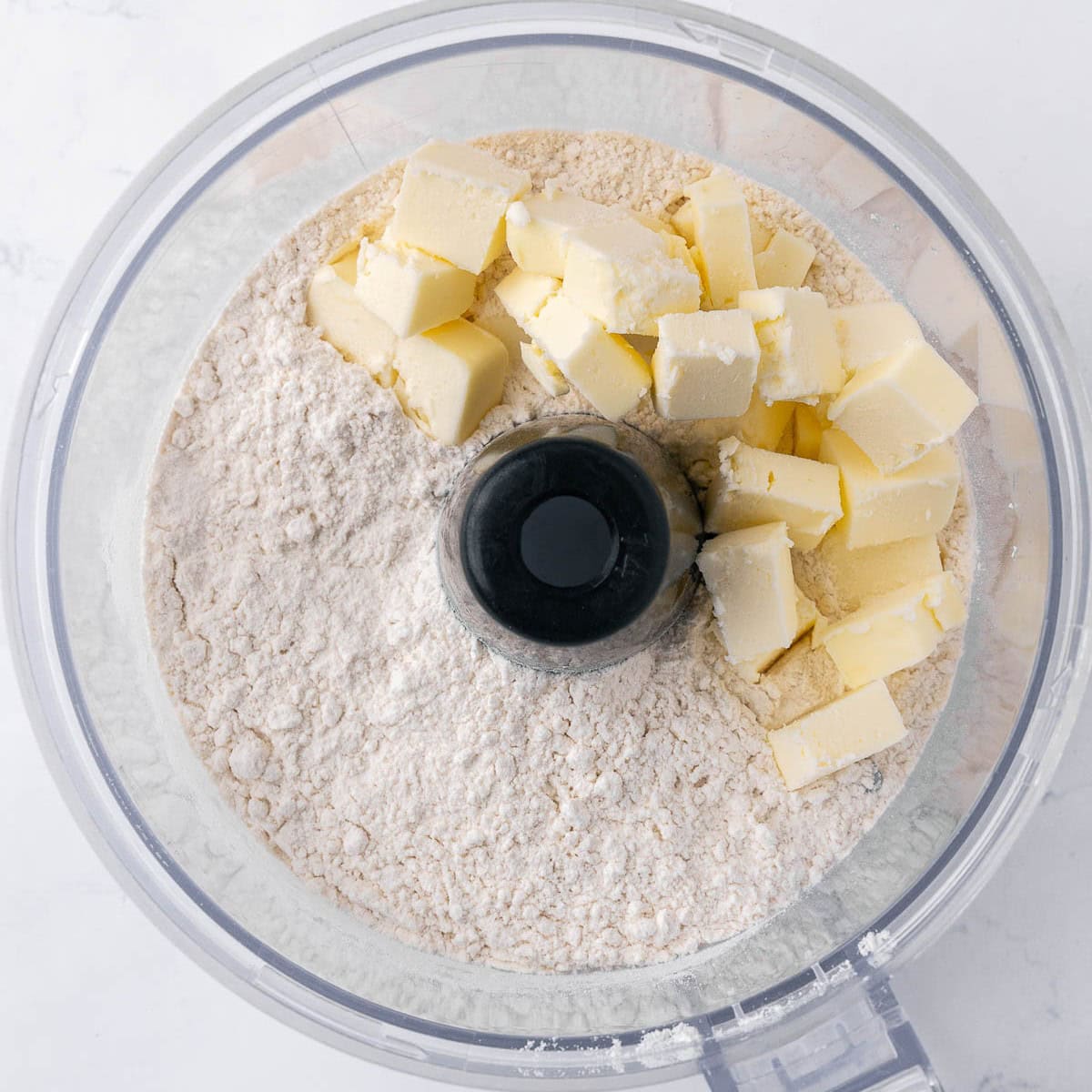 Flour, sugar, and salt in the bowl of a food processor after pulsing with butter cubes added.