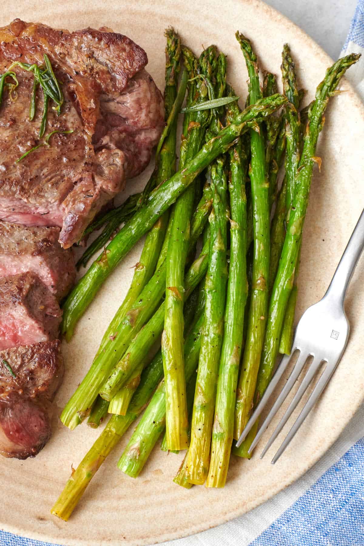 Air fryer asparagus on a plate with sliced steak.