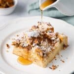 Slice of French toast casserole on a plate with syrup being poured over.