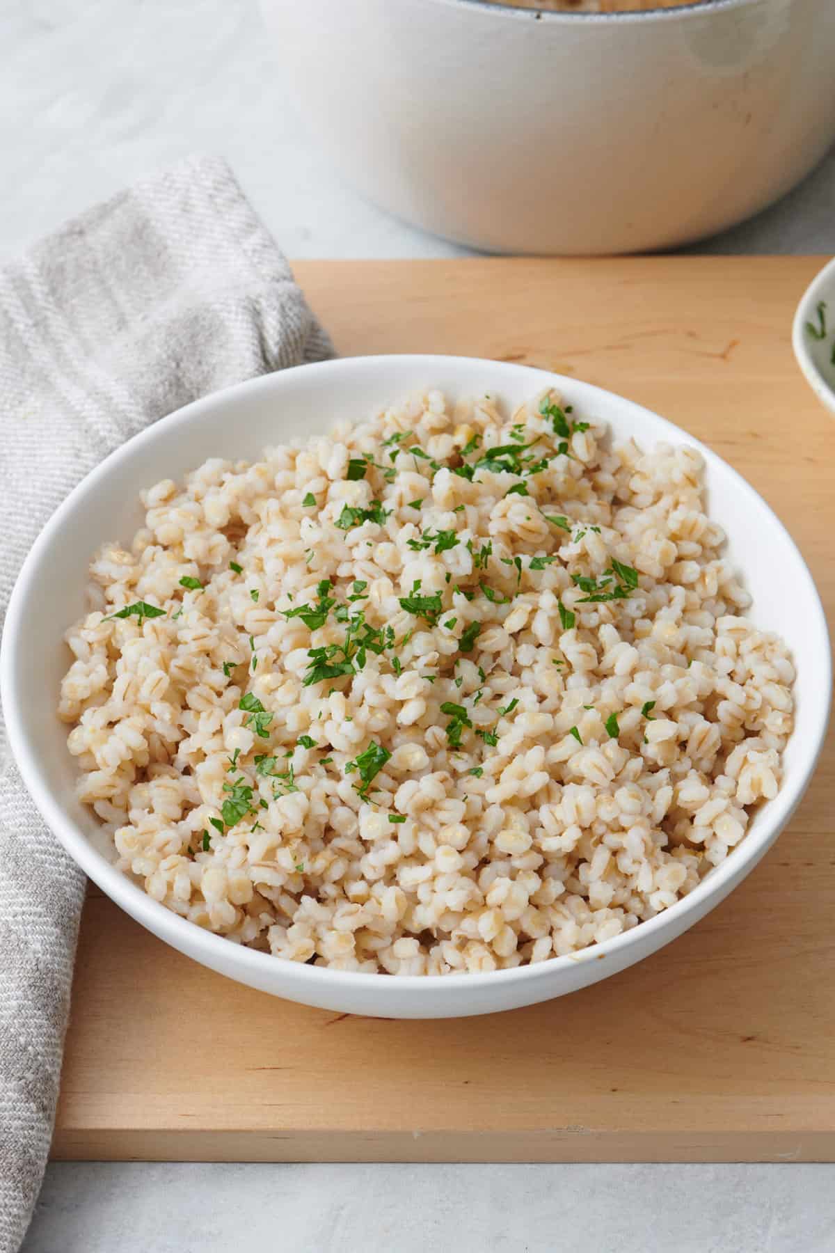 Cooked barley in a bowl on top of kitchen board and garnished with fresh parsley.