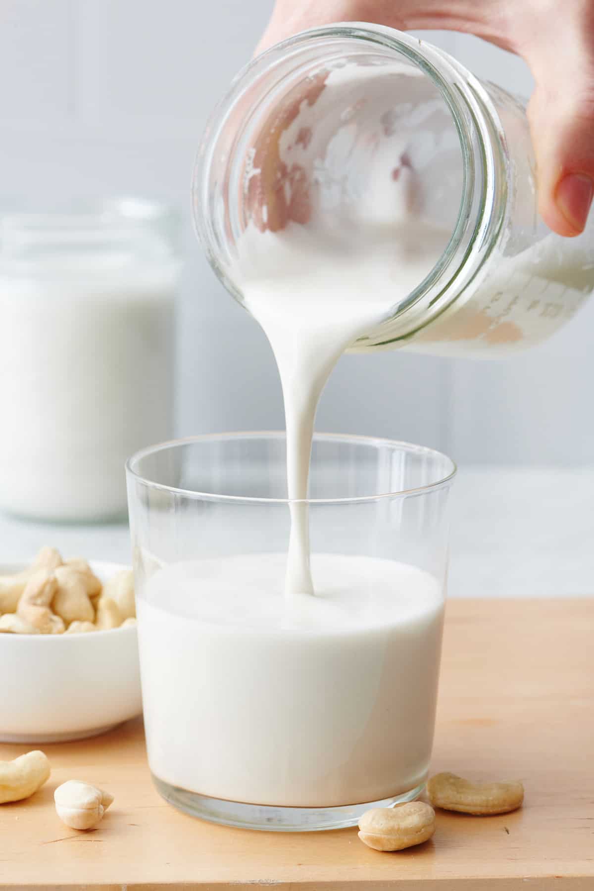Pouring homemade cashew milk into a glass.