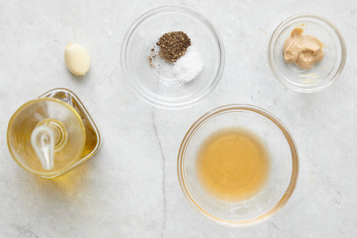 Base ingredients for making recipe: oil, garlic clove, salt and pepper, dijon mustard, and vinegar.