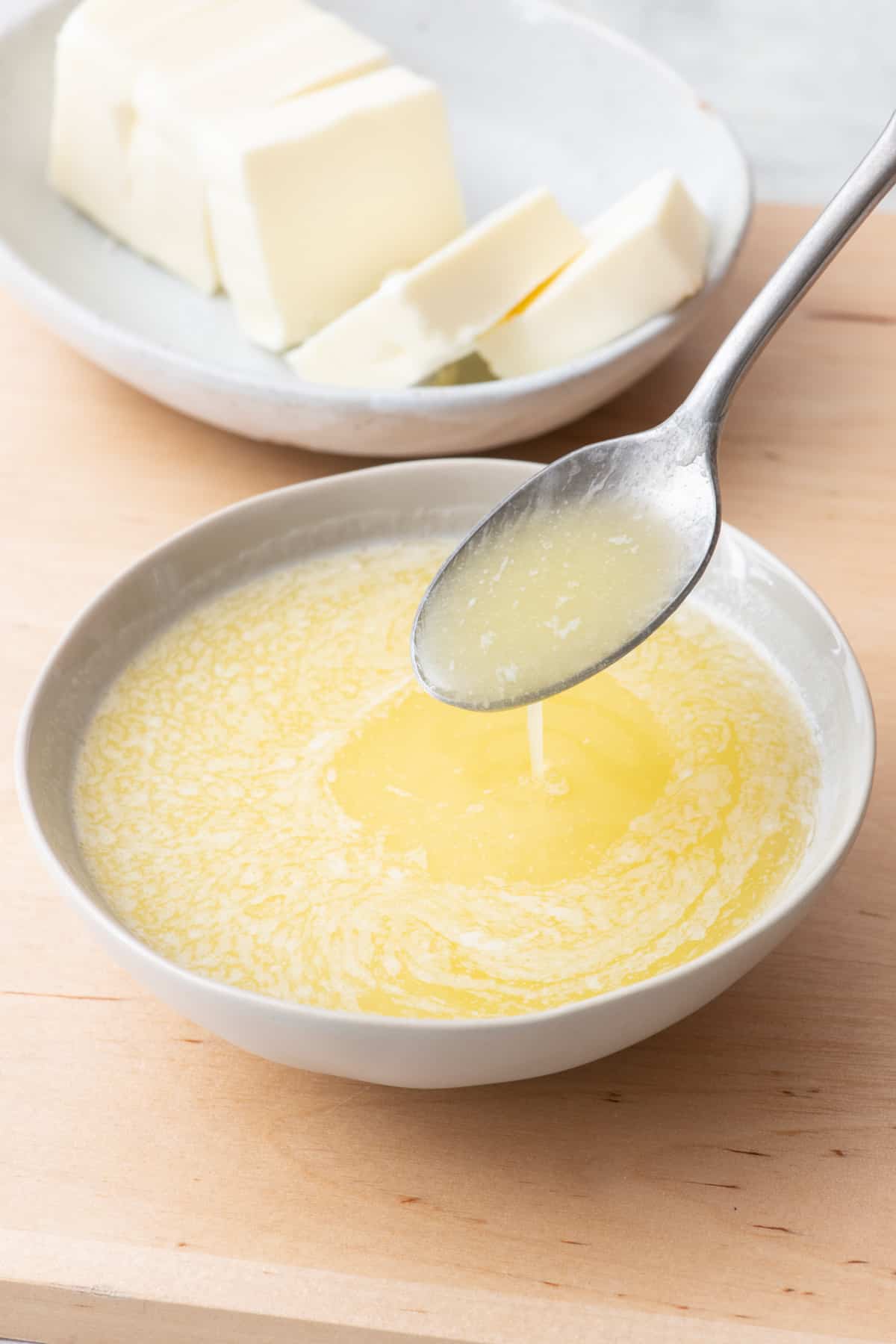 Melted butter in a bowl with a spoon lifting some up and a stick of butter nearby.
