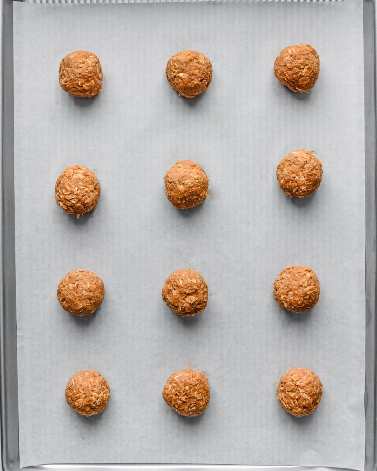 Cookie dough balls on a parchment lined baking sheet before baking.