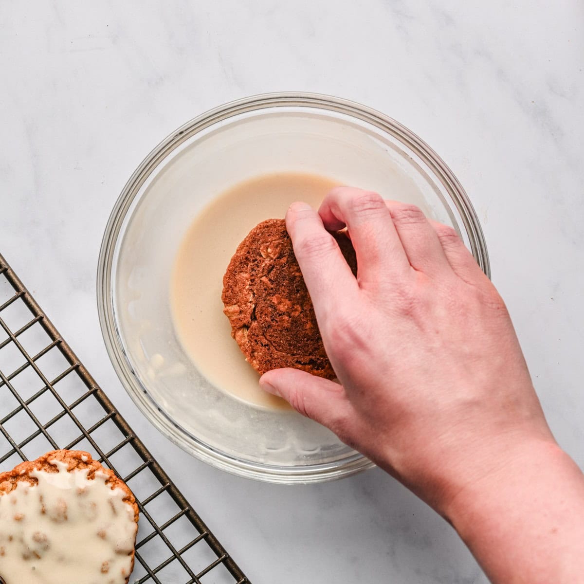 Hand dipping a cooled cookie into the icing.