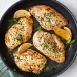 Lemon garlic chicken breasts in a skillet with lemon wedges.