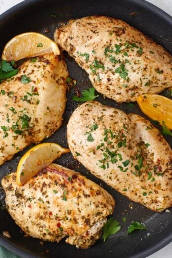 Lemon garlic chicken breasts in a skillet with lemon wedges.