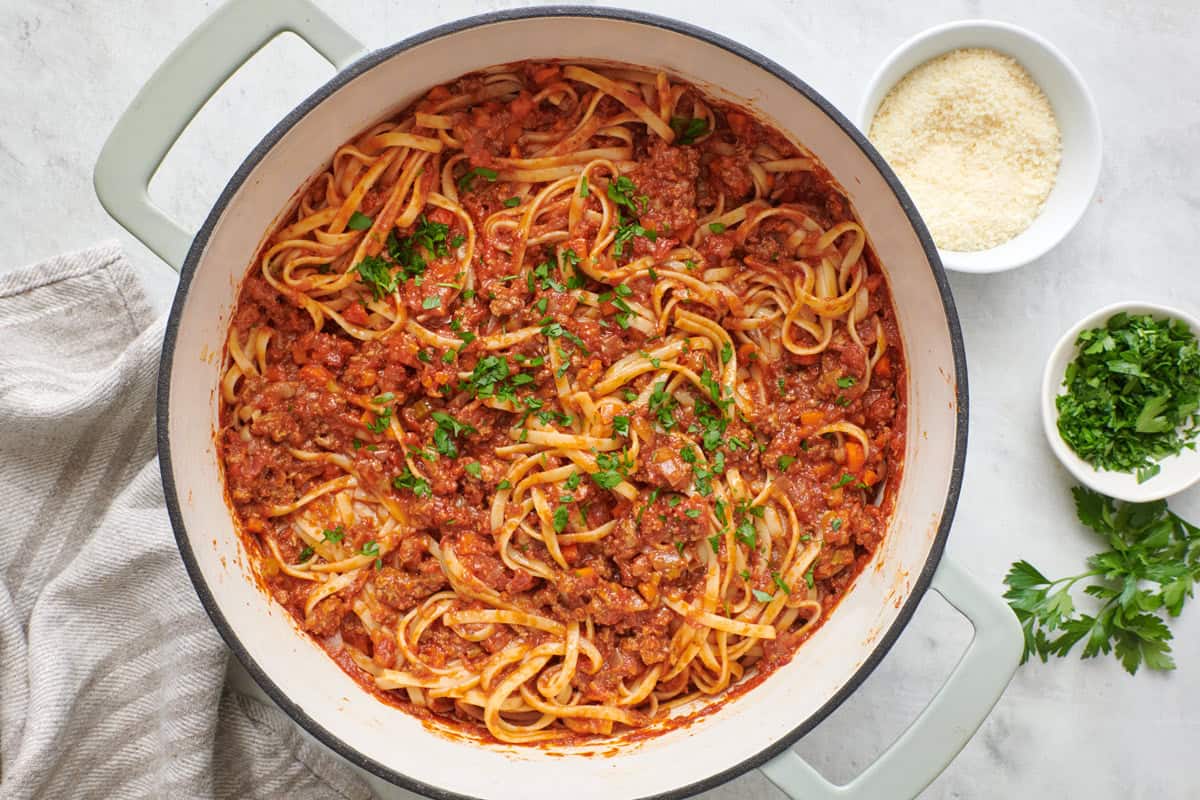 Pasta Bolognese in a large pan topped with fresh basil leaves with a wooden spoon