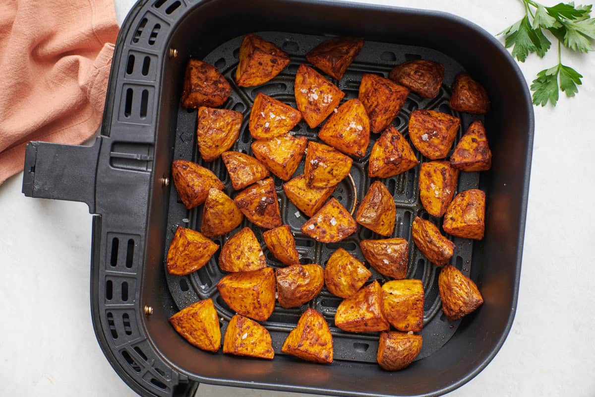 Cubed potatoes in an air fryer basket after frying up crispy, garnished with flaky salt.