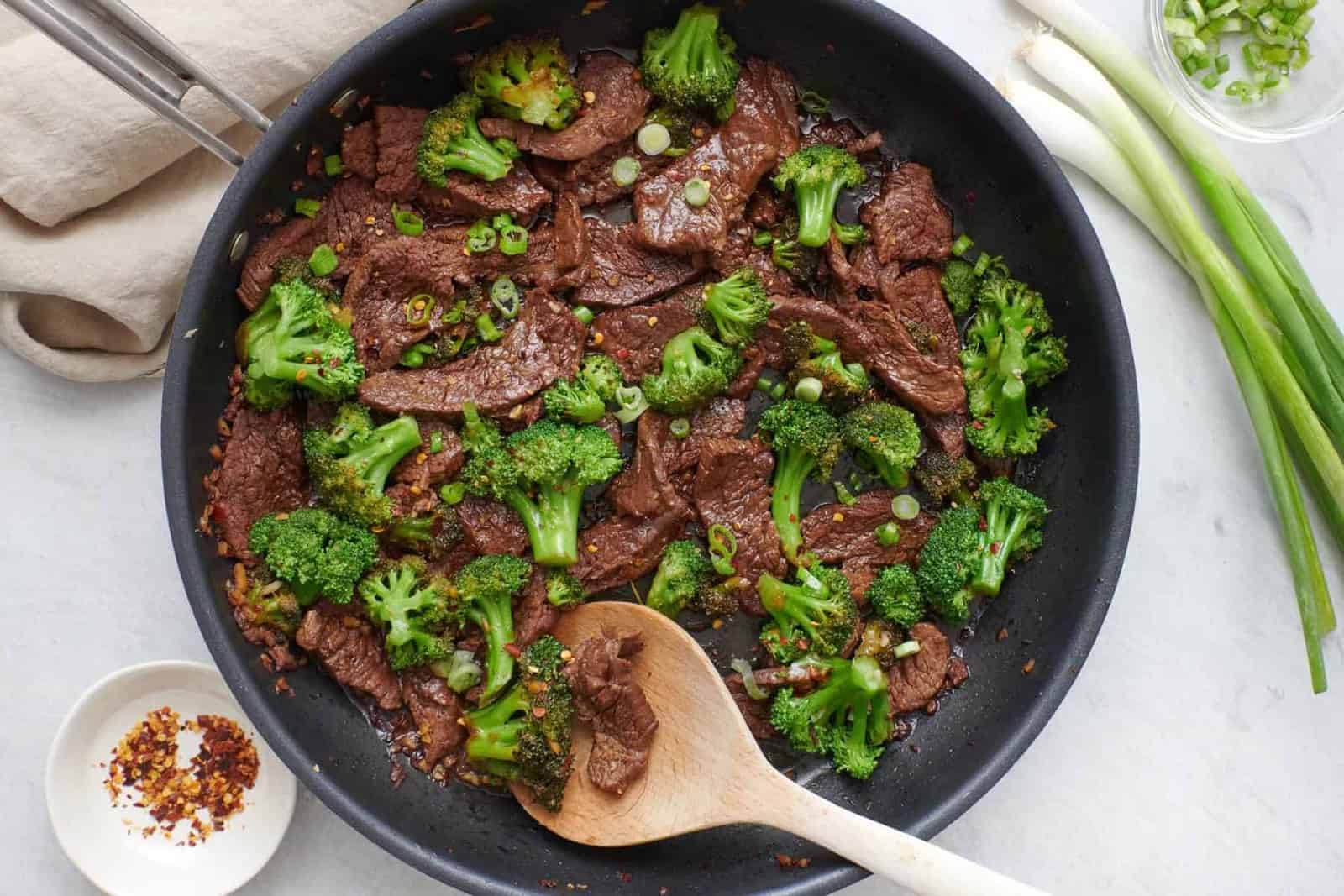 Beef and broccoli stir fry in skillet with a wooden spoon dipped in.