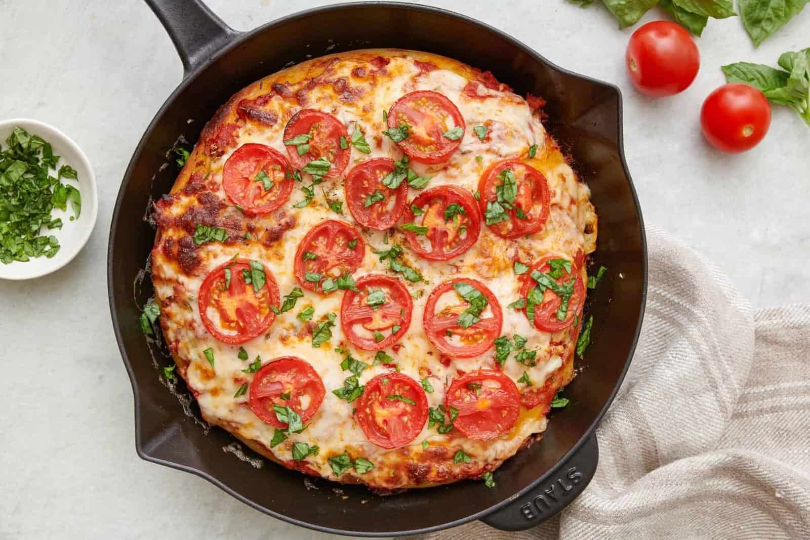 Cast iron pizza in skillet garnished with fresh chopped basil.