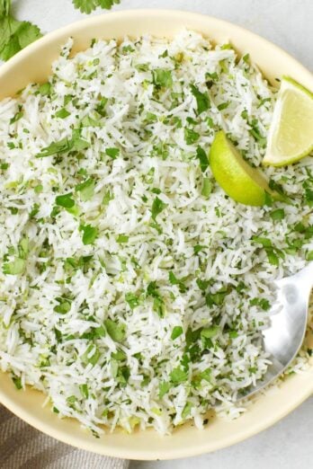 Cilantro lime rice in a bowl with a few lemon wedges and a spoon dipped in.