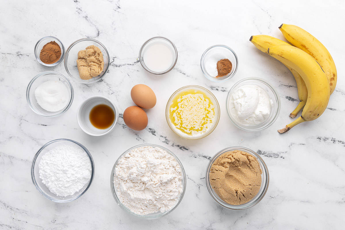 Ingredients for cinnamon swirl banana bread: Ripe bananas, light brown sugar, melted butter, Greek yogurt, eggs, vanilla extract, all-purpose flour, baking soda, ground cinnamon, salt, granulated sugar, powdered sugar, and milk.