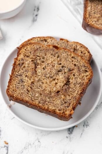 A white plate with 2 slices of cinnamon swirl banana bread on it.