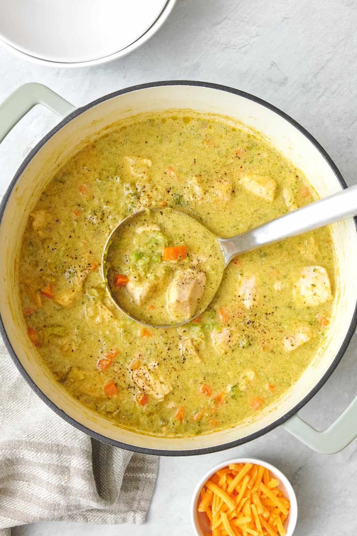 Creamy chicken broccoli soup in a pot with a ladle lifting some up.